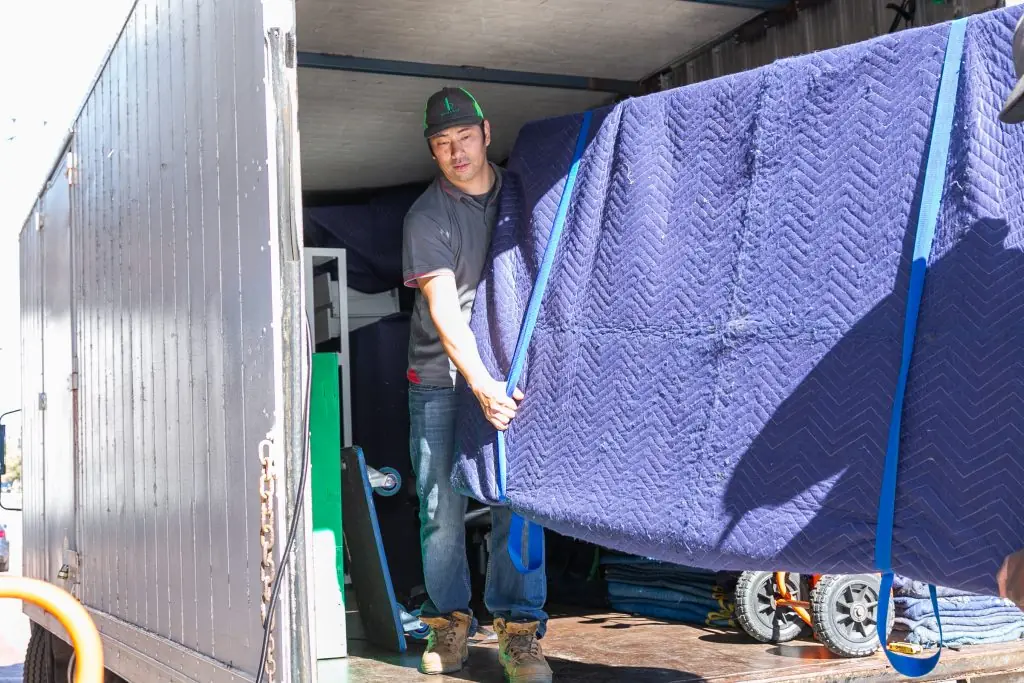 Removalist loading blanket-wrapped furniture onto a tailgate truck in Perth