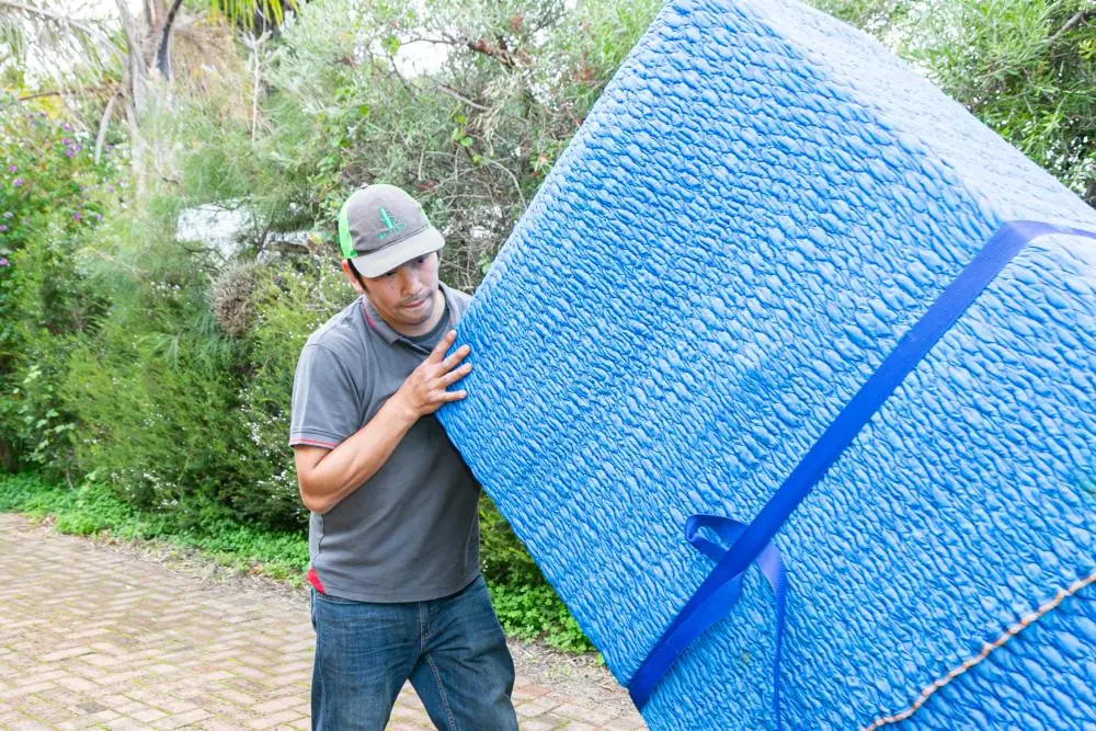 Mover carrying a large blanket-wrapped item secured with blue straps